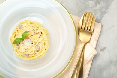 Photo of Plate with delicious pasta Carbonara and cutlery on grey textured table, flat lay