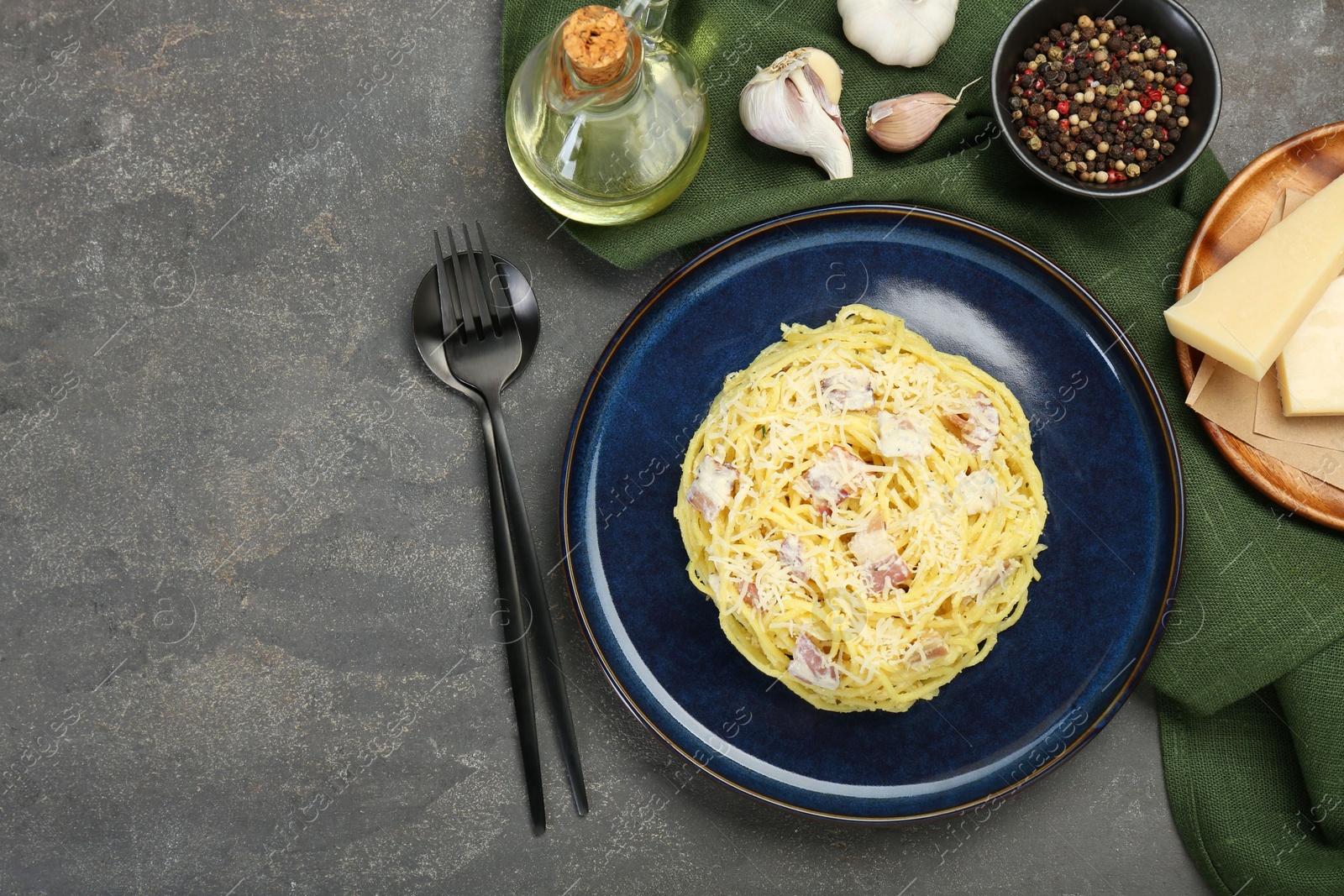 Photo of Plate with delicious pasta Carbonara, products and cutlery on grey textured table, flat lay. Space for text