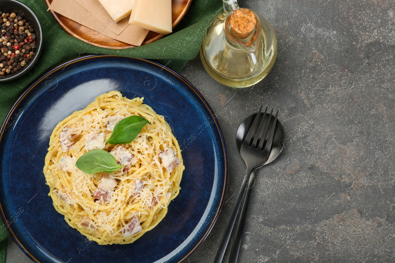 Photo of Plate with delicious pasta Carbonara, products and cutlery on grey textured table, flat lay. Space for text