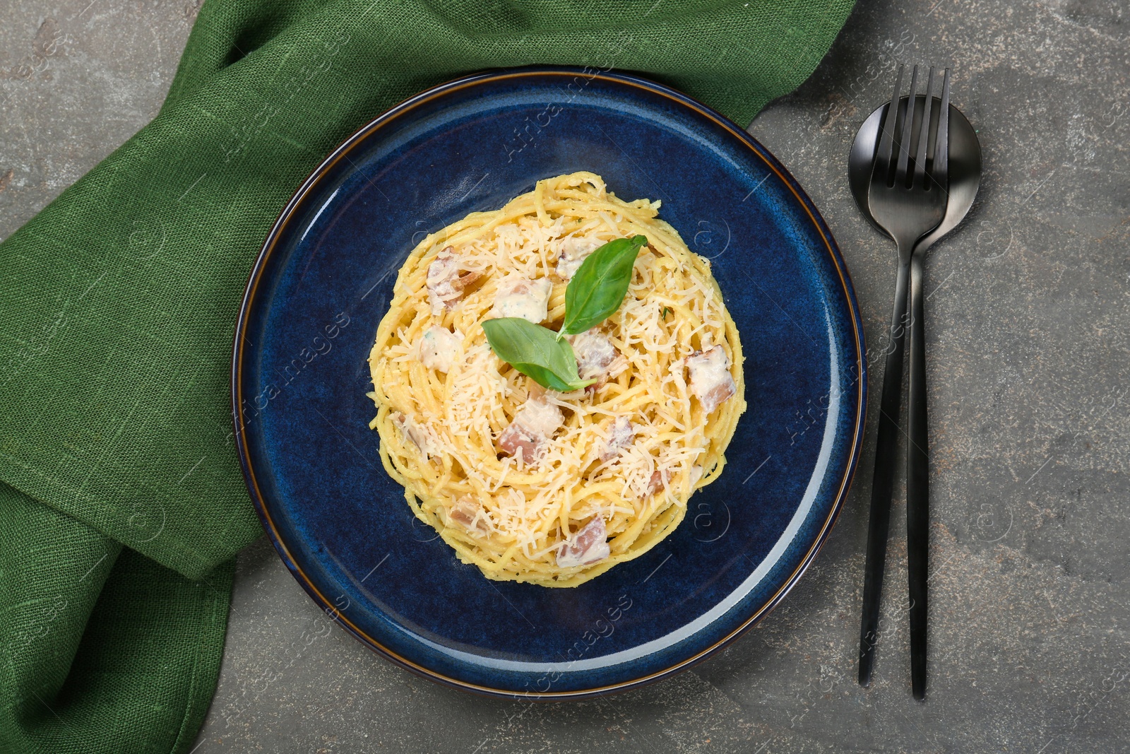 Photo of Plate with delicious pasta Carbonara and cutlery on grey textured table, flat lay