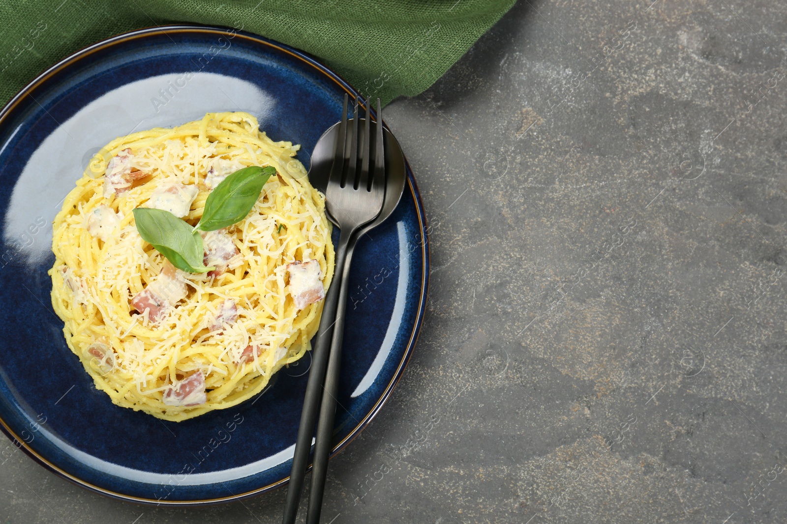 Photo of Plate with delicious pasta Carbonara and cutlery on grey textured table, top view. Space for text