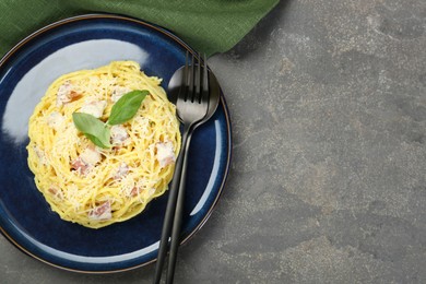 Photo of Plate with delicious pasta Carbonara and cutlery on grey textured table, top view. Space for text