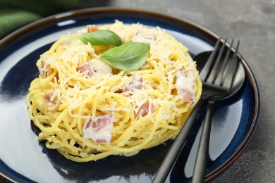 Photo of Plate with delicious pasta Carbonara and cutlery on grey textured table, closeup