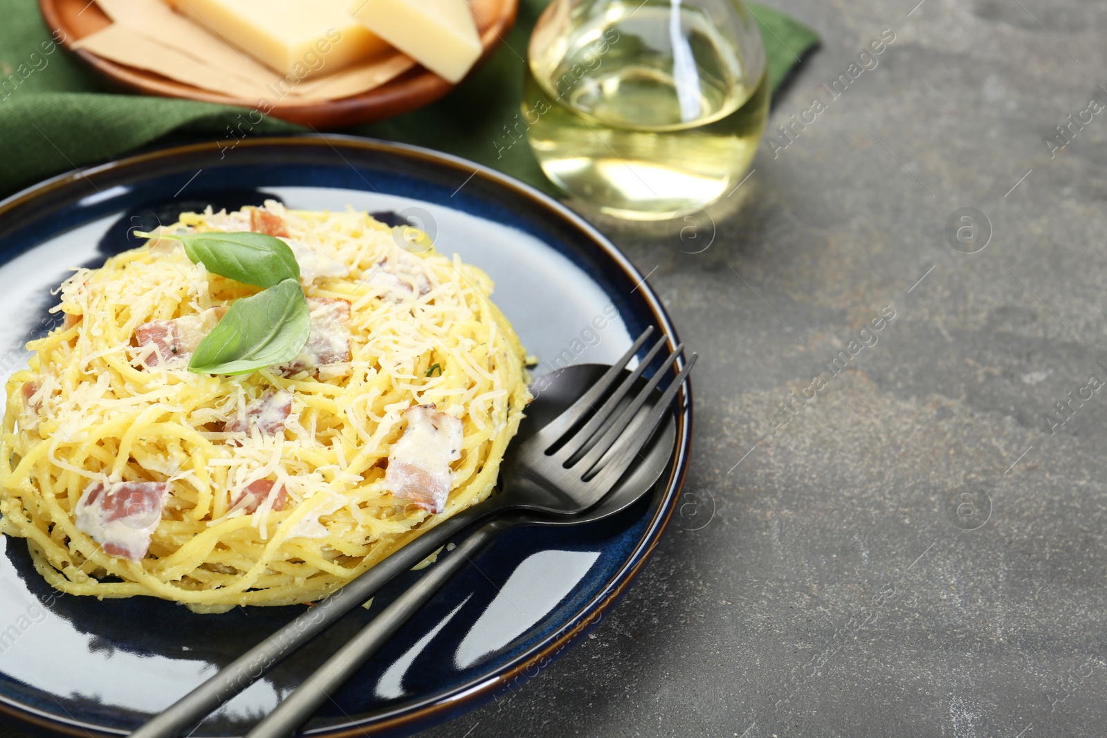 Photo of Plate with delicious pasta Carbonara and cutlery on grey textured table, closeup. Space for text