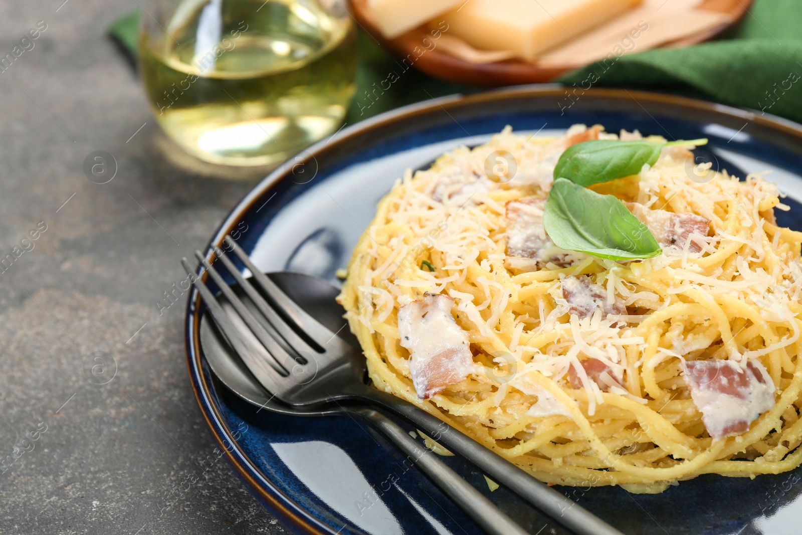 Photo of Plate with delicious pasta Carbonara and cutlery on grey textured table, closeup. Space for text