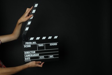 Photo of Woman with clapperboard on black background, closeup. Space for text