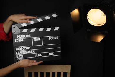 Photo of Woman with clapperboard near spotlight on black background, closeup