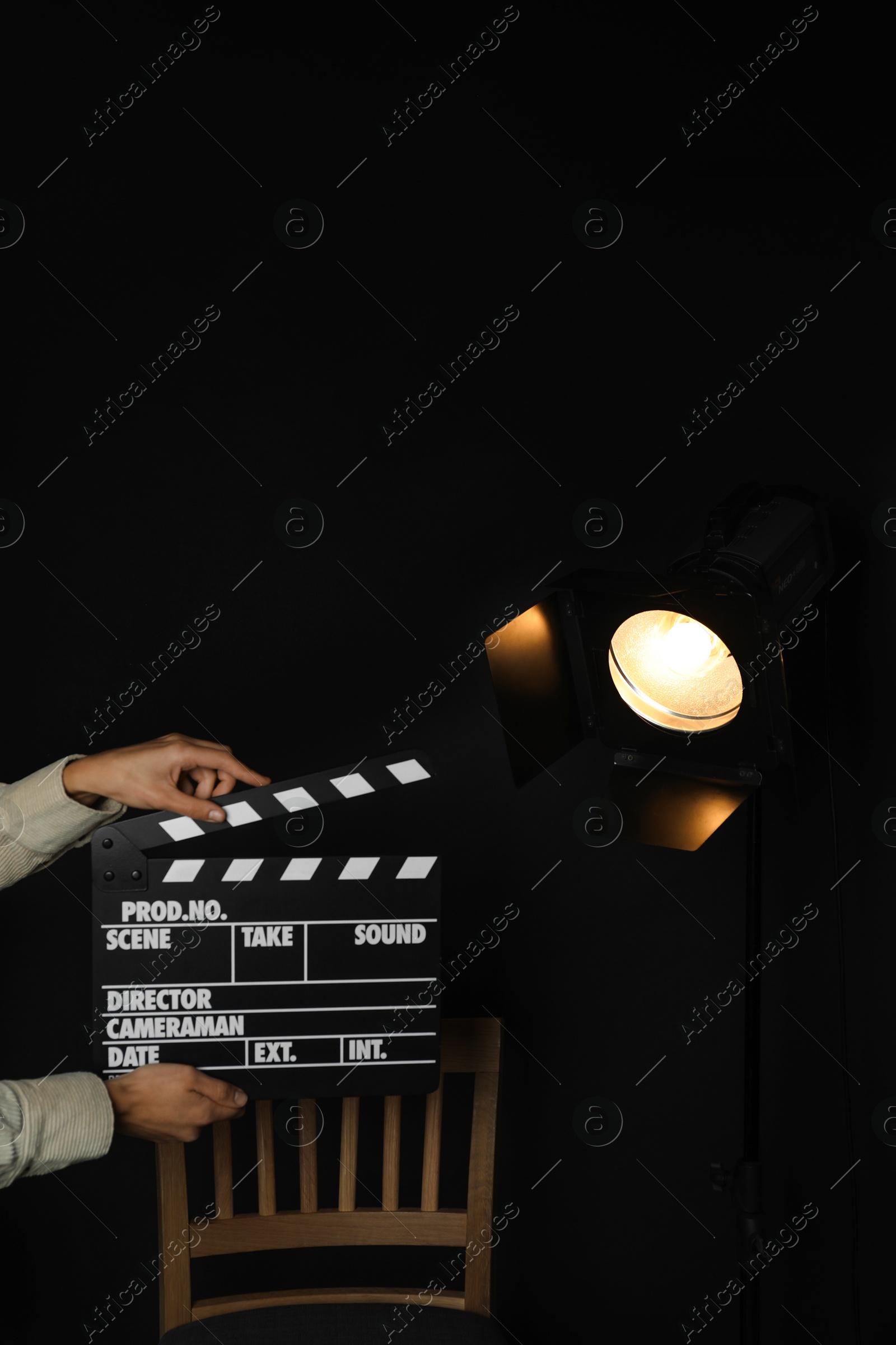 Photo of Woman with clapperboard near spotlight on black background, closeup