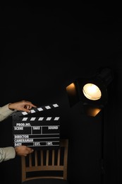 Photo of Woman with clapperboard near spotlight on black background, closeup