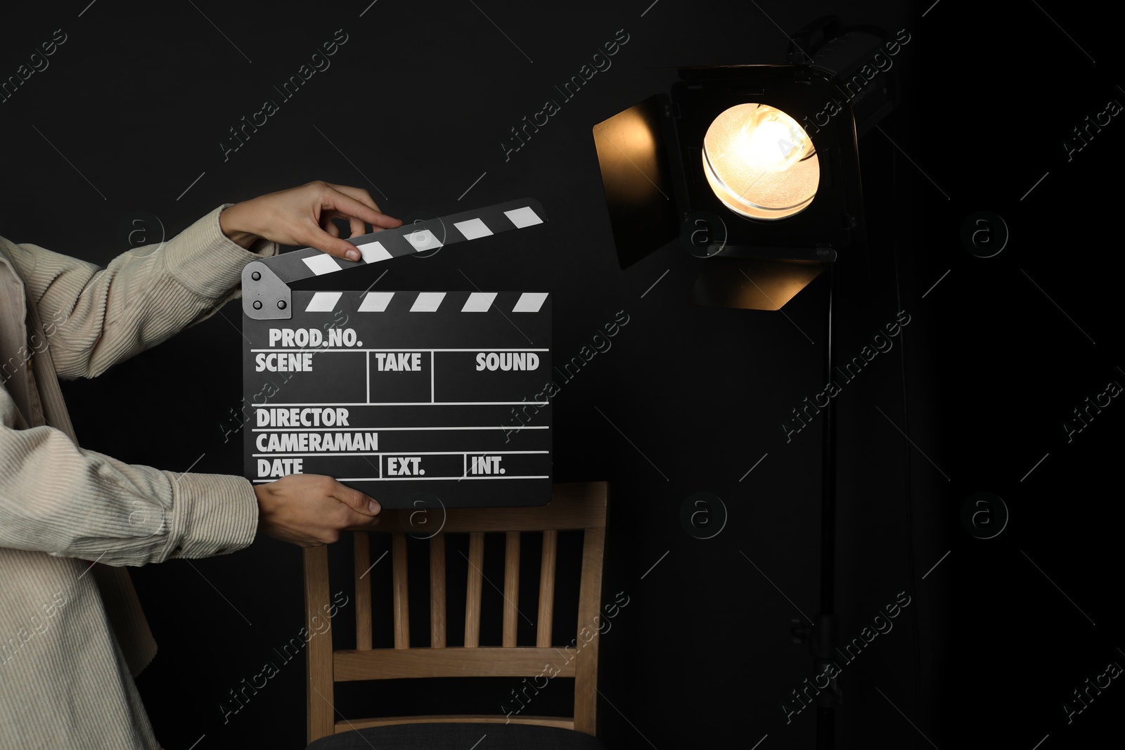 Photo of Woman with clapperboard near spotlight on black background, closeup