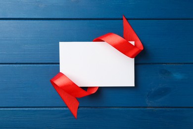 Blank card and red ribbon on blue wooden table, top view