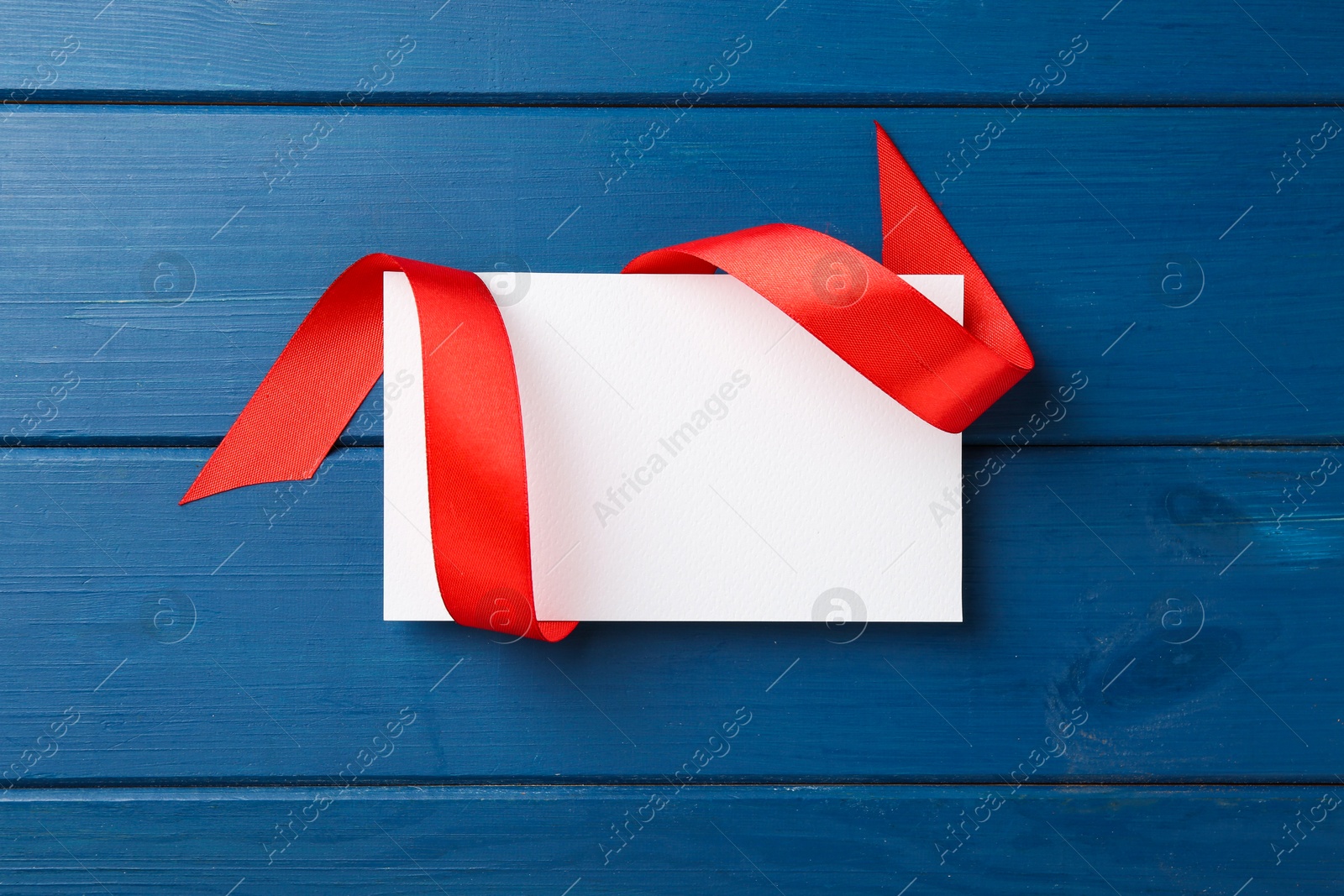 Photo of Blank card and red ribbon on blue wooden table, top view