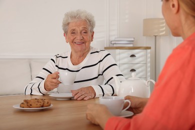 Caregiver and senior woman enjoying hot drink at table indoors