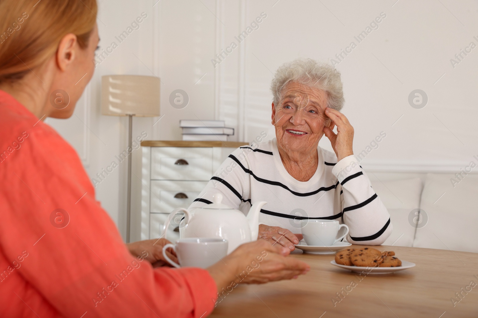 Photo of Caregiver and senior woman enjoying hot drink at table indoors