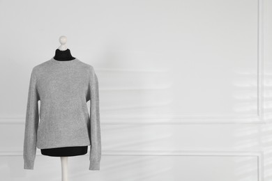 Photo of One female mannequin with sweater near light wall. Space for text