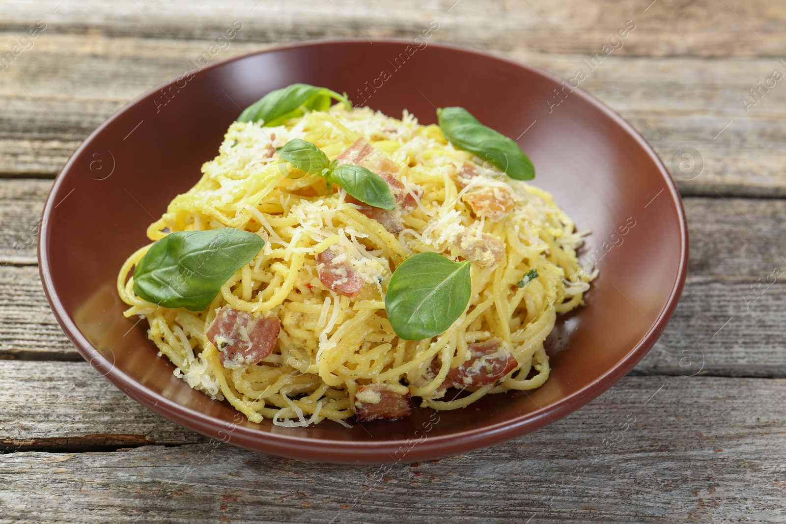 Photo of Delicious pasta Carbonara in bowl on wooden table, closeup