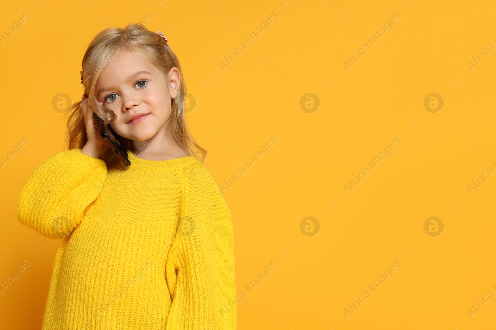 Photo of Cute little girl talking on smartphone against orange background, space for text