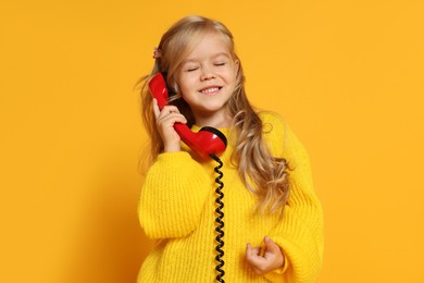 Photo of Cute little girl with handset of telephone on orange background