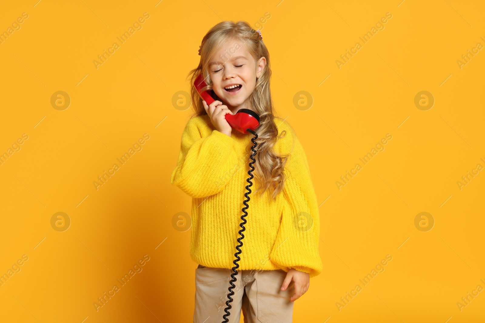 Photo of Cute little girl with handset of telephone on orange background