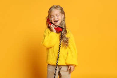 Photo of Cute little girl with handset of telephone on orange background