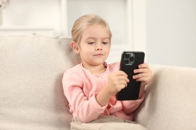 Cute little girl using smartphone on sofa at home