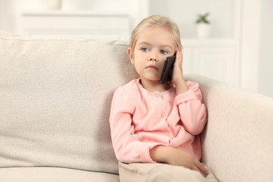 Photo of Cute little girl talking on smartphone at home, space for text