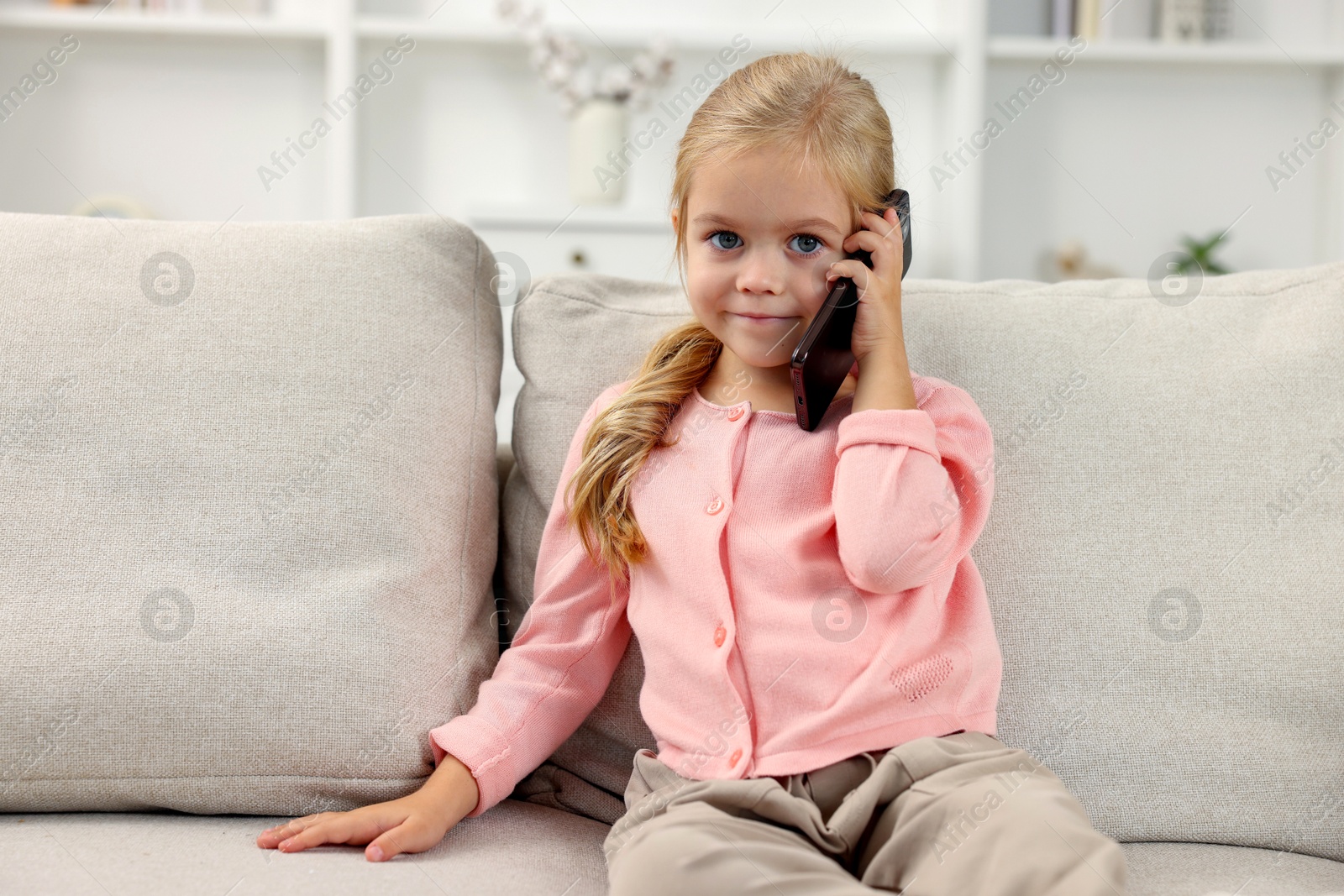 Photo of Cute little girl talking on smartphone at home