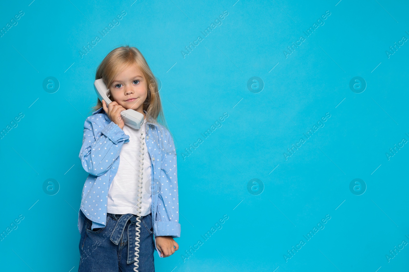 Photo of Cute little girl with handset of telephone on light blue background, space for text