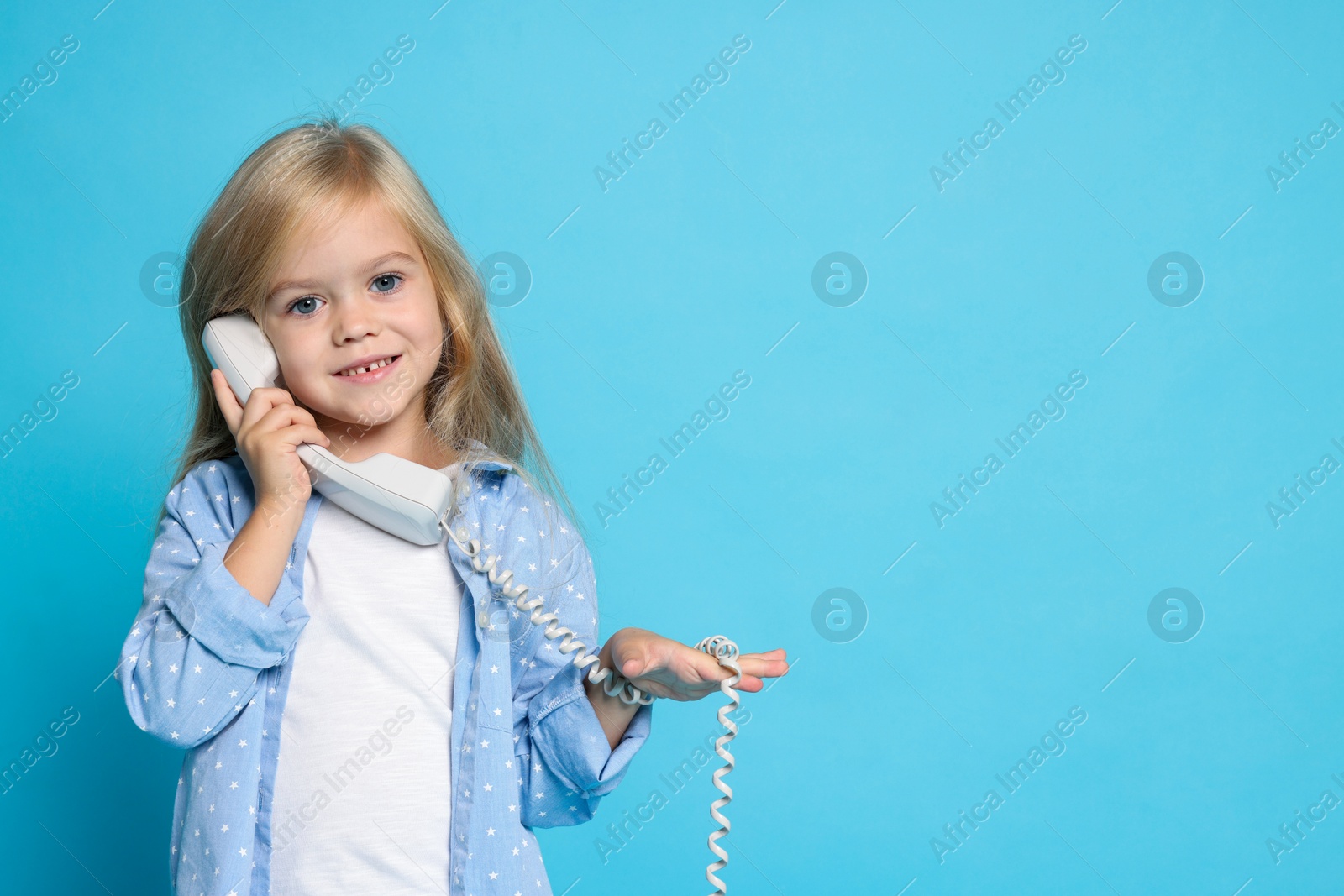 Photo of Cute little girl with handset of telephone on light blue background, space for text