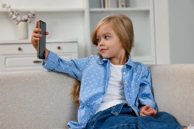 Photo of Cute little girl using taking selfie on sofa at home