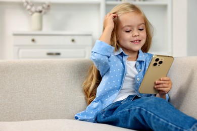 Photo of Cute little girl using smartphone on sofa at home