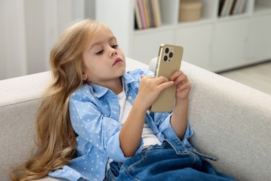 Photo of Cute little girl using smartphone on sofa at home