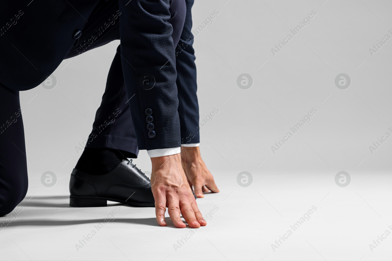 Photo of Businessman in starting position for run on light grey background, closeup. Space for text