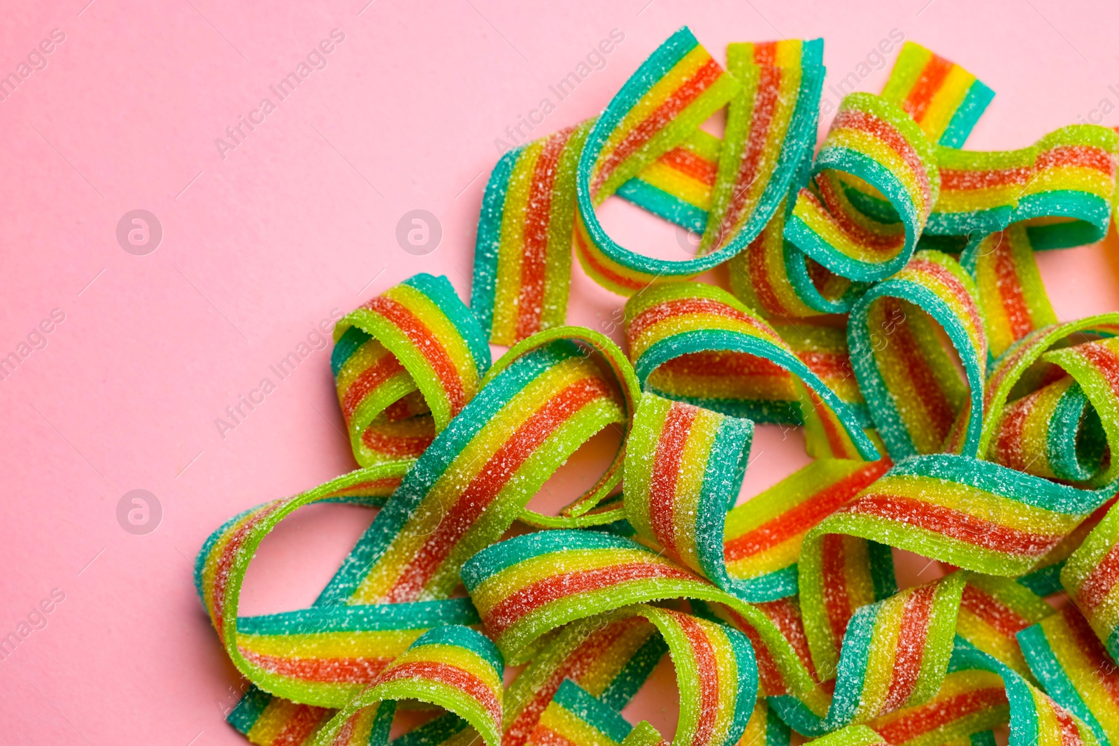 Photo of Tasty rainbow sour belts on pink background, top view