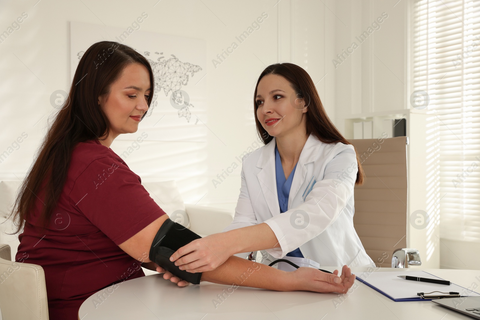 Photo of Nutritionist measuring overweight woman's blood pressure at desk in hospital