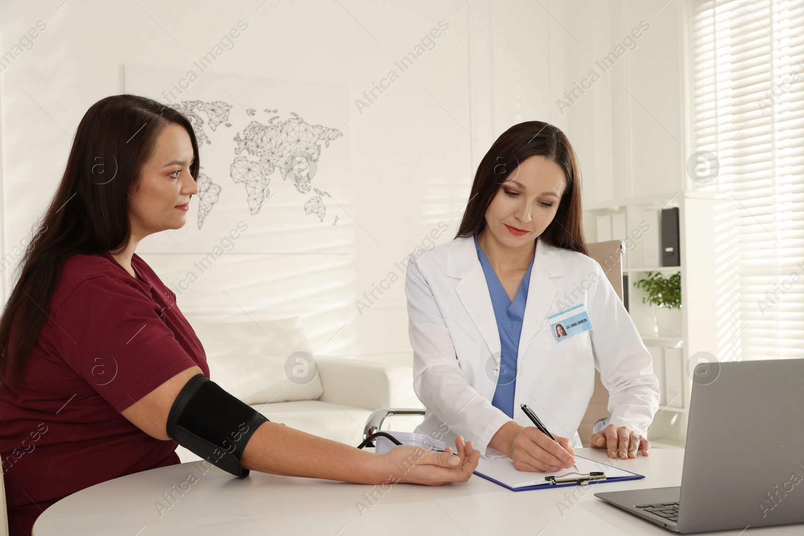 Photo of Nutritionist measuring overweight woman's blood pressure at desk in hospital