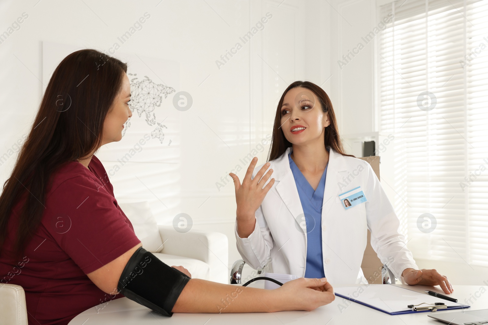 Photo of Nutritionist measuring overweight woman's blood pressure at desk in hospital