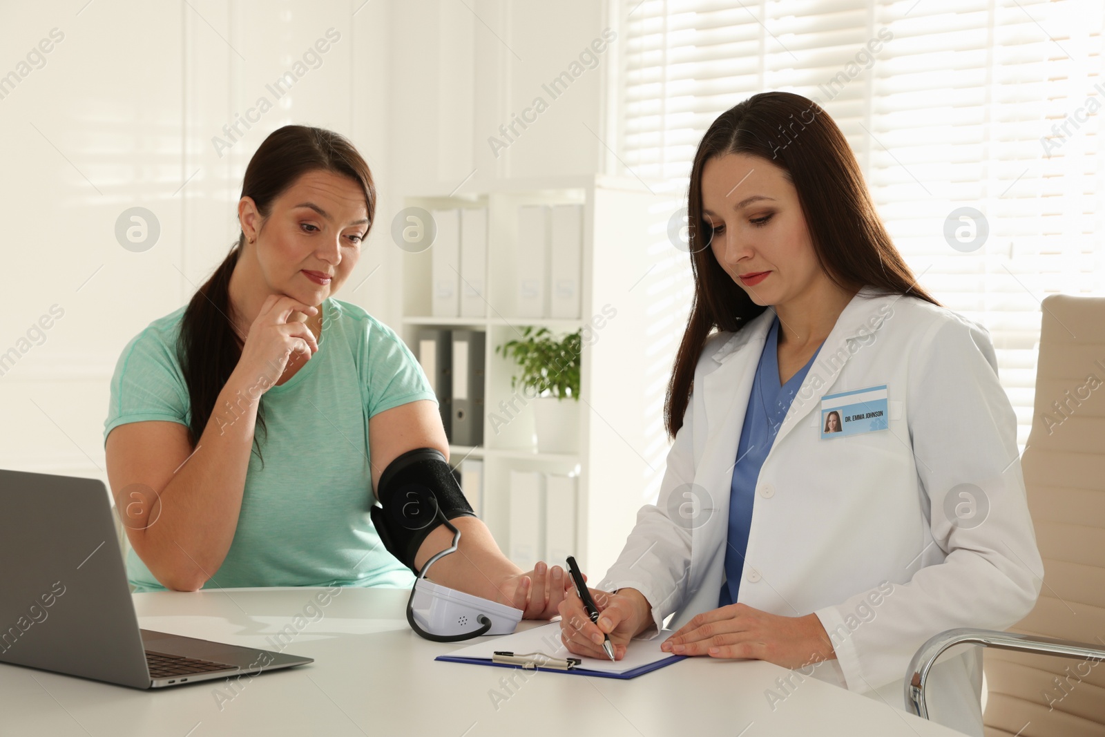 Photo of Nutritionist measuring overweight woman's blood pressure at desk in hospital