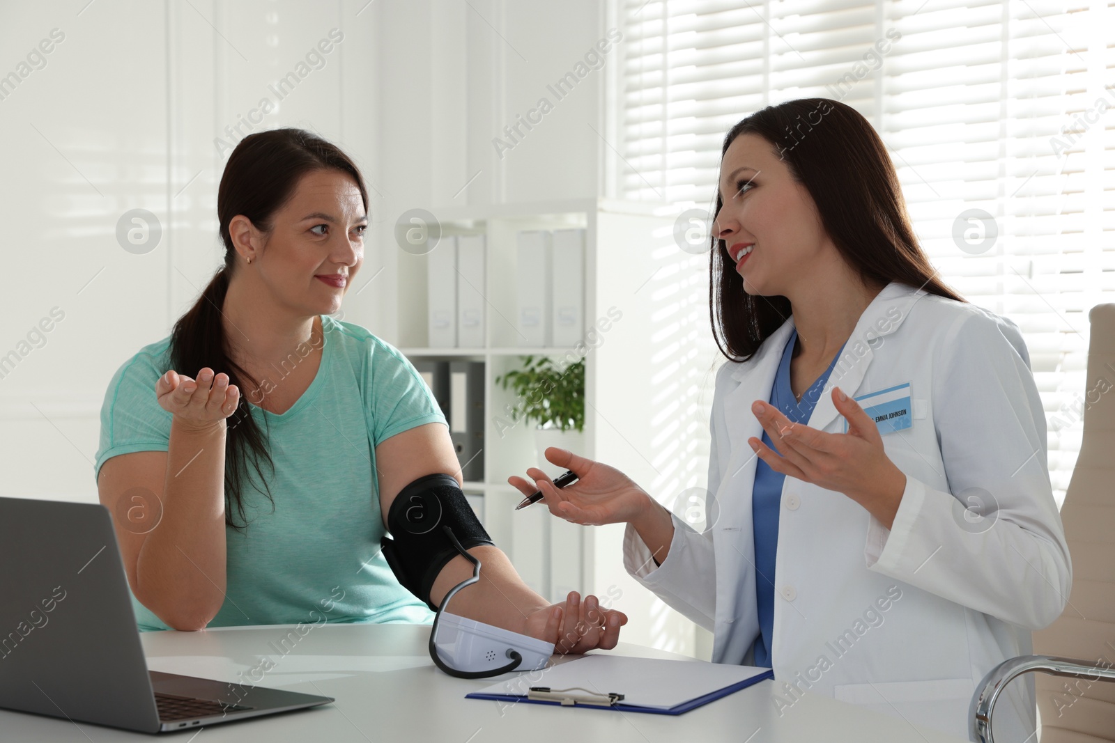 Photo of Nutritionist measuring overweight woman's blood pressure at desk in hospital