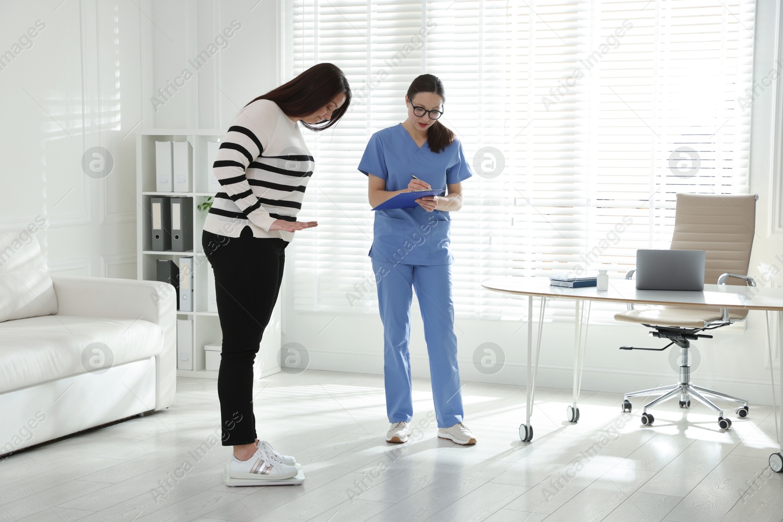 Photo of Nutritionist measuring plus size woman's weight in hospital