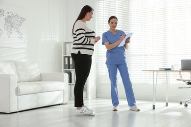 Photo of Nutritionist measuring plus size woman's weight in hospital