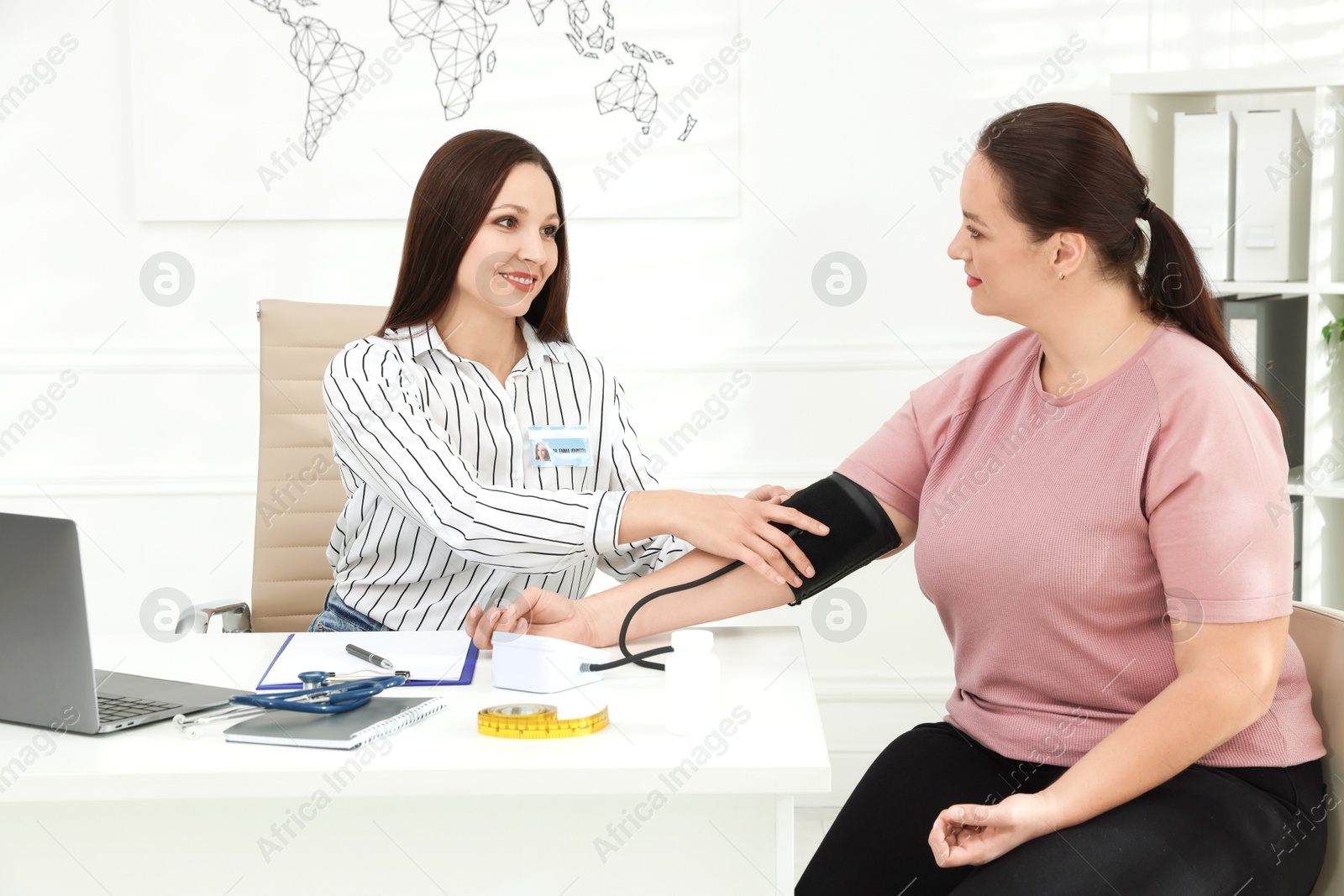 Photo of Nutritionist measuring overweight woman's blood pressure at desk in hospital