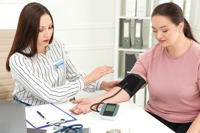 Photo of Nutritionist measuring overweight woman's blood pressure at desk in hospital