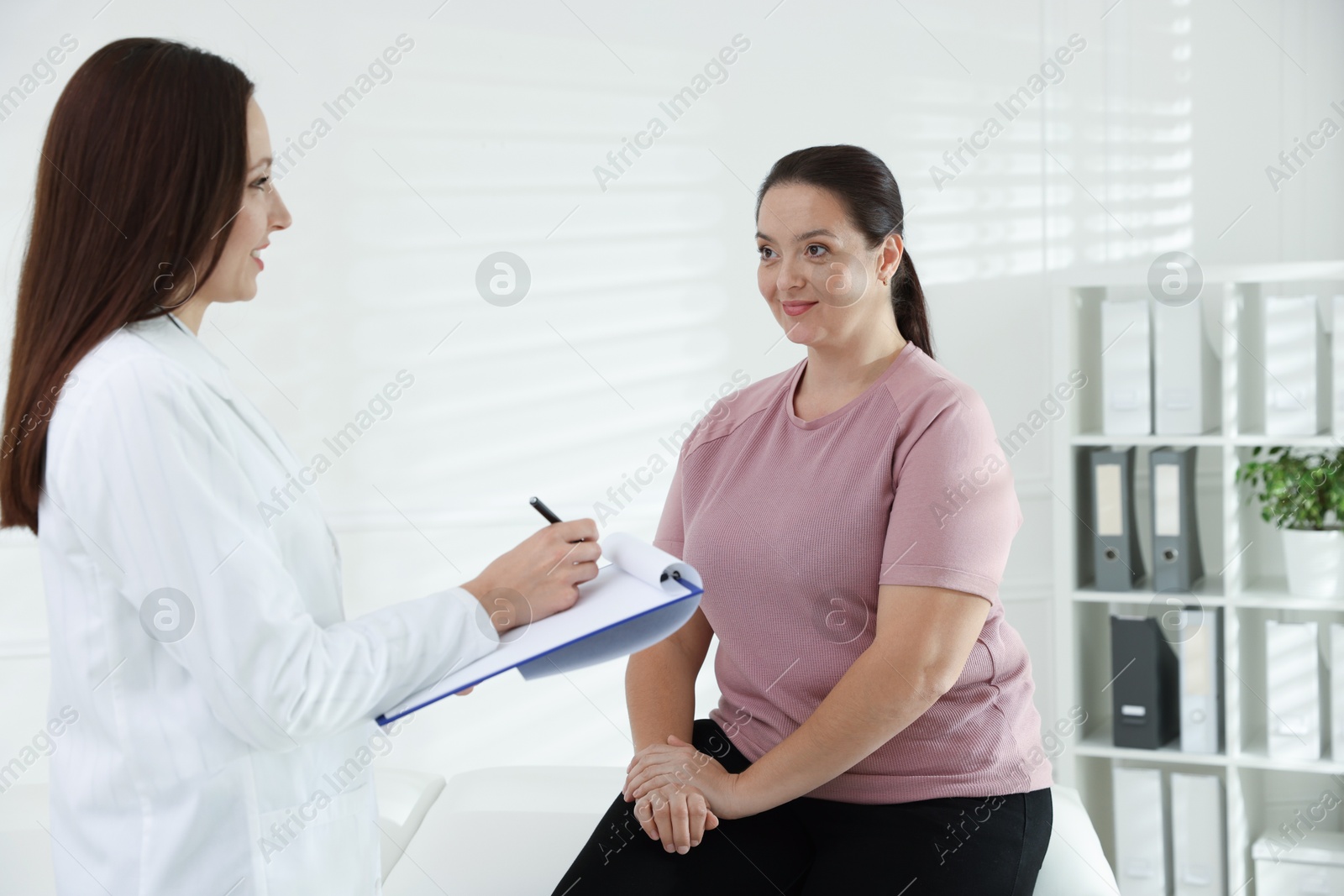 Photo of Nutritionist with clipboard giving recommendations to overweight woman in hospital