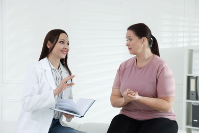 Photo of Nutritionist with notebook giving recommendations to overweight woman in hospital