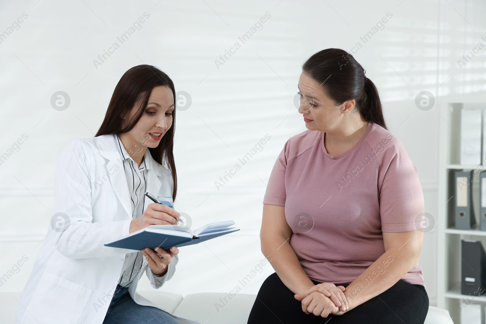 Photo of Nutritionist with notebook giving recommendations to overweight woman in hospital