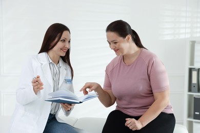 Photo of Nutritionist with notebook giving recommendations to overweight woman in hospital