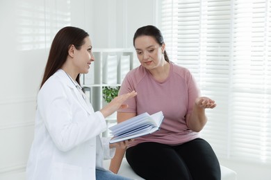 Photo of Nutritionist with notebook giving recommendations to overweight woman in hospital