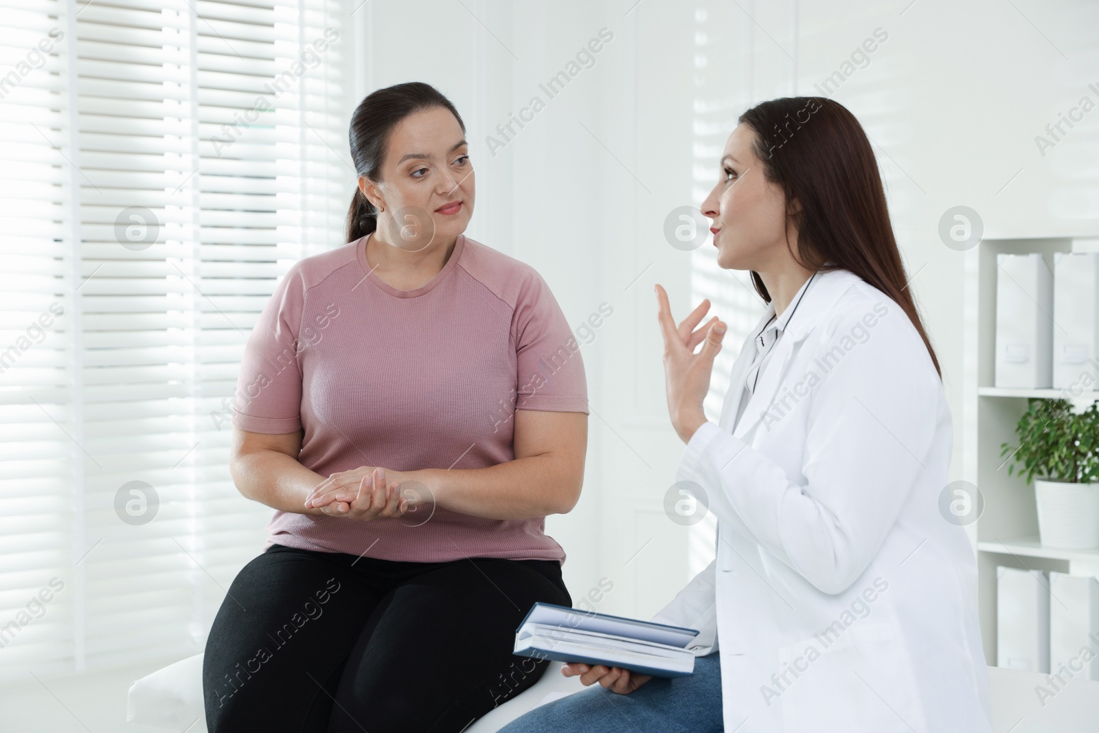 Photo of Nutritionist with notebook giving recommendations to overweight woman in hospital