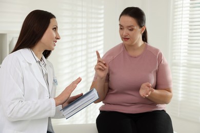 Photo of Nutritionist with notebook giving recommendations to overweight woman in hospital